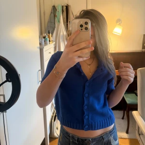 Blå kofta från Zara - Säljer en snygg blå kofta från Zara med korta ärmar och knappar framtill. Perfekt för en stilren look. Koftan är ribbad vid ärmslut och nederkant vilket ger en fin passform. Aldrig andvänd.