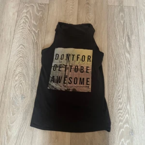 Svart ärmlös topp med tryck - Säljer en svart ärmlös topp med texttryck 'DONT FORGET TO BE AWESOME' på framsidan. Perfekt för en avslappnad stil. Toppen är i ett mjukt material och har en enkel design.