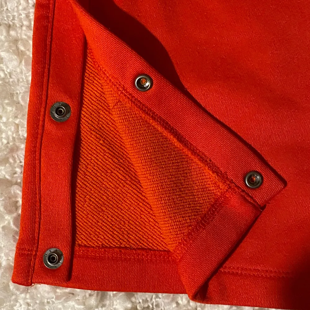 Snygga röda byxor från Champion med knappar längs sidorna och en bekväm resårmidja. Perfekta för en sportig look eller avslappnad stil. Byxorna har även snörning i midjan för extra justering.. Farkut & Housut.