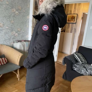 Svart dunjacka från Canada Goose - Säljer en svart dunjacka från Canada Goose med pälsdetaljer på huvan, köpt från Thernlunds kvitto finns. Jackan har en lång passform. Den har en dragkedja och knappar framtill samt en ikonisk logga på ärmen. Kan gå ner i pris vid snabb affär. Skriv för fler bilder