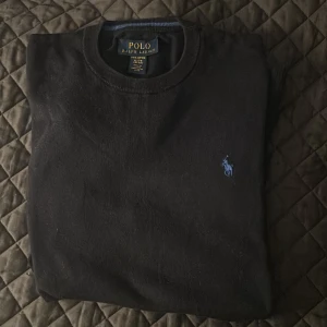 Svart tröja från Polo Ralph Lauren - Säljer en klassisk svart tröja från Polo Ralph Lauren i mjuk pima bomull. Tröjan har en broderad logotyp i blått på bröstet och rund halsringning. Perfekt för en stilren look. Säljer den för att den tyvärr är för liten för mig. Är i väldigt bra skick utan några defekter 8/10. Är i barnspråks XL vilket motsvarar S