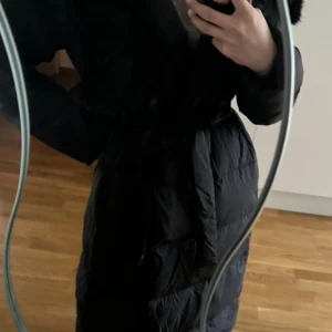 Svart lång dunjacka med bälte - Snygg och varm svart lång dunjacka från Luxe Duckdown. Jackan har ett bälte i midjan för en figursydd look och långa ärmar. Perfekt för kalla dagar med sin quiltade design. Jackan är från Luxeswe, storlek S men passar även XS och M. Köpte för 3499 kronor och säljer för 2499 kronor. Har aldrig använt jackan, säljer jackan för att jag har hittat en annan som är mer passande för mig.