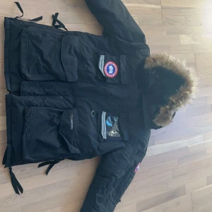 Canada goose jacka - Säljer en svart parkajacka från Canada Goose med pälsfodrad huva och flera praktiska fickor. Jackan har en broderad logotyp på bröstet och är perfekt för kalla vinterdagar. Den är tillverkad i slitstarkt material och har en klassisk design. Rensar min garderob nu efter vintern den är sjukt varm, bra pris pågrund av att jag vill bli av med den så fort som möjligt.