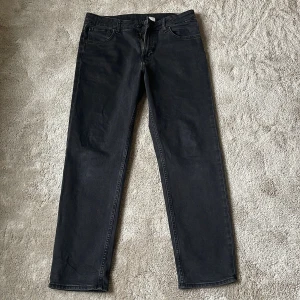 Svarta jeansbyxor från H&M - Snygga svarta jeansbyxor från H&M med relaxed fit och justerbar midja. Byxorna har en tapered leg och klassisk femficksdesign med dragkedja och knapp framtill. Perfekta för en avslappnad stil.