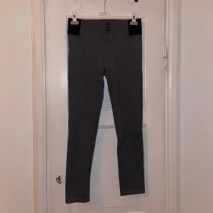 Grå byxor med knappar - Snygga grå byxor med hög midja och knappar framtill. Byxorna har en tight passform och är perfekta för en stilren look. De är tillverkade i ett mjukt och stretchigt material för extra komfort.