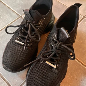 Svarta sneakers från Steve Madden - Snygga svarta sneakers från Steve Madden med stickad ovandel och snörning. Skorna har en modern design med märkets logga på sidan och en bekväm sula. Perfekta för en stilren look. Storlek 40. Endast använda inomhus ett fåtal ggr. I mycket bra skick. Originalkartong medföljer.