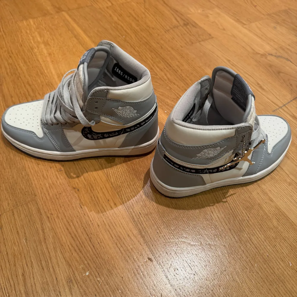 Exklusiva sneakers i samarbete mellan Nike och Dior. Skorna har en stilren design i grått och vitt med Dior-logotypen på swooshen. Högt skaft med snörning och perforerad tå för extra ventilation. Perfekta för den som vill ha något unikt och trendigt men även lite lyx. . Kengät.