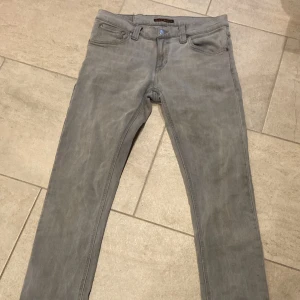 Grå jeans från Nudie Jeans - 🔥🔥🔥Snygga grå jeans från Nudie Jeans med en klassisk femficksdesign. De har en tight passform och är tillverkade i ett slitstarkt denimtyg. Perfekta för en stilren look. Storlek 30/32🔥🔥🔥