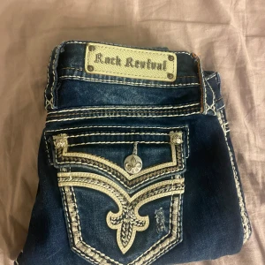 Mörkblå jeans från Rock Revival - Snygga mörkblå jeans från Rock Revival med unika broderade detaljer på bakfickorna. Jeansen har lågmidjade passform och sitter ganska löst.💞Priset kan diskuteras