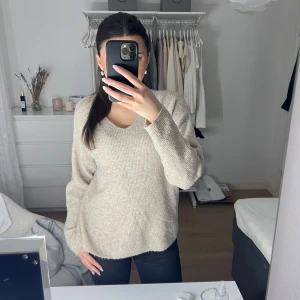 Beige stickad tröja - Säljer en mysig beige stickad tröja med v-ringning. Perfekt för kyliga dagar med sin mjuka och bekväma passform. Tröjan har långa ärmar och en neutral färg som passar till det mesta. Ett måste i garderoben för höst och vinter!