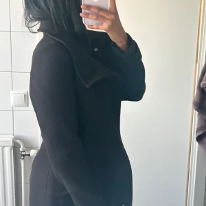 Svart kappa - Snygg svart kappa med en stilren design. Perfekt för kyligare dagar med sin långa ärm och klassiska look. Passar bra till både vardag och mer uppklädda tillfällen.