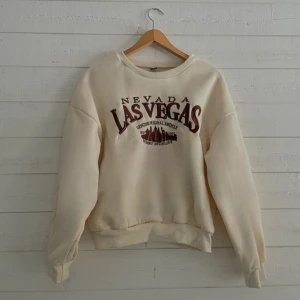 Beige sweatshirt med Las Vegas-tryck - Säljer en beige sweatshirt med tryck av 'Nevada Las Vegas' i brunt. Tröjan har en avslappnad passform och långa ärmar. Perfekt för en casual look.