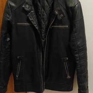 Svart skinnjacka från Livergy - Snygg svart skinnjacka från Livergy med dragkedja och flera fickor med dragkedjor. Jackan har en klassisk look med långa ärmar och en stilren design. Perfekt för en cool och avslappnad stil.