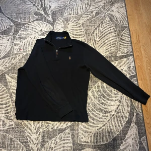 Svart tröja från Ralph Lauren - Säljer en stilren svart tröja från Ralph Lauren med dragkedja vid halsen. Endast använd ett fåtal gånger och är storlek M. Skicket är 9/10.