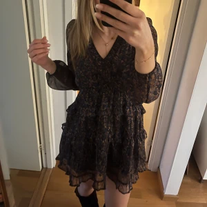 Klänning från Neo Noir - Säljer en superfin blommig klänning från Neo Noir.🤩 Den har ett super fint mönster med blåa, bruna och lite guld inslag på blommor. Den har en v-ringad design med långa ärmar och volangdetaljer. Super fint skick och använt bara fåtals gånger, säljer då den inte kommer till användning💕