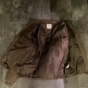 Brun pufferjacka från New Garments - Säljer en brun pufferjacka från New Garments i storlek M. Jackan har en quiltad design och är perfekt för kyligare väder. Den har långa ärmar och en bekväm passform. Perfekt för att hålla dig varm och stilren.