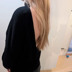 Svart ribbad tröja med öppen rygg - Snygg svart ribbad tröja med en unik öppen ryggdesign. Tröjan har långa ärmar och en bekväm passform, perfekt för en stilren look. Passar bra till både jeans och kjol.