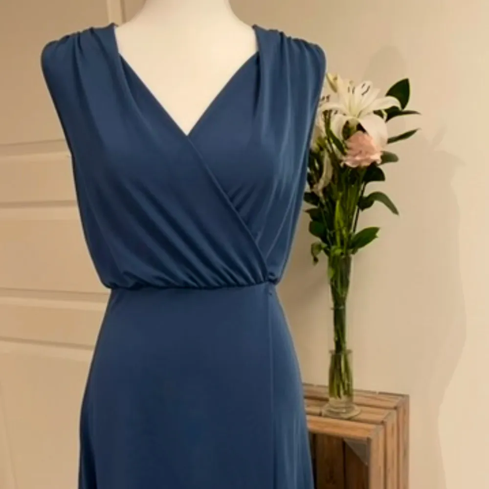 Elegant blå omlottklänning från Nümph med v-ringad design. Klänningen är ärmlös och har en mjuk, flödande passform som ger en stilren look. Perfekt för både vardag och speciella tillfällen.. Mekot.