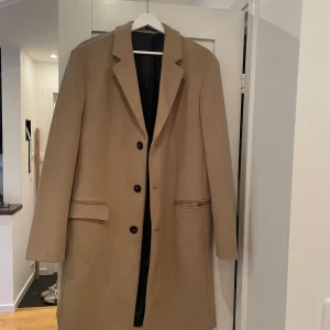 Beige kappa - Beige kappa med klassisk design och knappar framtill. Använd 2 gånger. Märke Zara storlek L