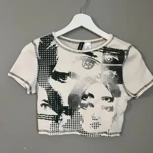 Säljer en cool vit croppad t-shirt från H&M Divided med ett unikt svart tryck av ansikten. T-shirten har korta ärmar och en rund halsringning. Perfekt för en trendig look!