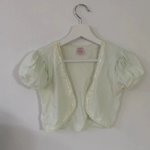 Ljusgrön bolerotopp med spetsdetaljer - Söt ljusgrön bolerotopp med korta puffärmar och spetsdetaljer längs kanterna. Perfekt för att lägga till en romantisk touch till din outfit. 💫