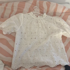 Vit blus från Holly & Whyte - Säljer en söt vit blus från Holly & Whyte med broderade blommor och hålmönster då den inte kommer till användning! Blusen har korta ärmar och en liten volang vid halsen. Perfekt för en somrig look! Skriv jättegärna för mer info❤️
