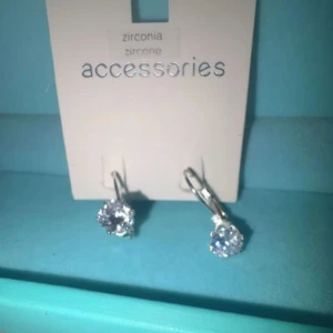 Silverfärgade örhängen med zirkonstenar - Eleganta silverfärgade örhängen med gnistrande zirkonstenar. Perfekta för att ge en touch av glamour till din look. Lätta att bära med en enkel krokdesign.