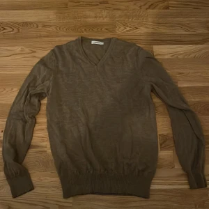 Beige tröja från J. Lindeberg - Säljer en stilren beige tröja från J. Lindeberg. Tröjan har en v-ringad design och är tillverkad i ett mjukt material. Perfekt för en avslappnad och elegant look.