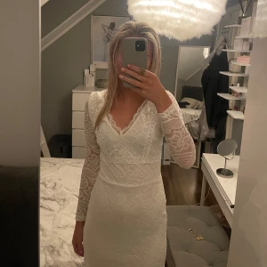 Vit spetsklänning med öppen rygg - Säljer en elegant vit spetsklänning med v-ringning och öppen rygg. Klänningen har långa ärmar och en figurnära passform som framhäver silhuetten. Perfekt för speciella tillfällen.
