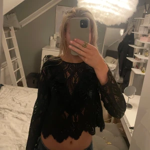 Svart spetsblus - Säljer en elegant svart spetsblus med långa ärmar och volangdetaljer. Blusen har ett vackert mönster och är perfekt för en stilfull look. Passar bra till både jeans och kjol.