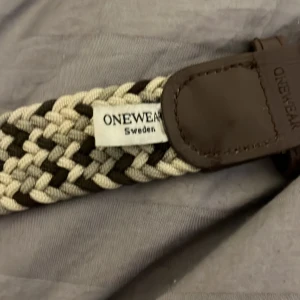 Flätat bälte från Onewear - Snyggt flätat bälte från Onewear i beige och brunt. Bältet har en stilren design med bruna skinnändar som ger en elegant touch. Perfekt för att lyfta vilken outfit som helst.