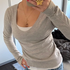 Grå v-ringad tröja - Säljer en stilren grå tröja med v-ringning. Tröjan har långa ärmar och ribbade muddar vid ärmslut och nederkant. Perfekt för en avslappnad och snygg look.