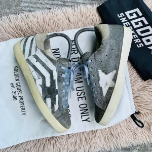 Grå sneakers från Golden Goose - Snygga grå sneakers från Golden Goose med vit stjärndetalj och randigt mönster på sidan. Skorna har ljusblå snörning och en krämfärgad sula. Perfekta för en avslappnad stil med en touch av unik design.