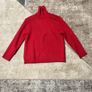 Röd ribbad polotröja - Snygg röd polotröja med ribbad design. Perfekt för kyligare dagar med sin höga krage och långa ärmar. En stilren och bekväm tröja som passar till många tillfällen.