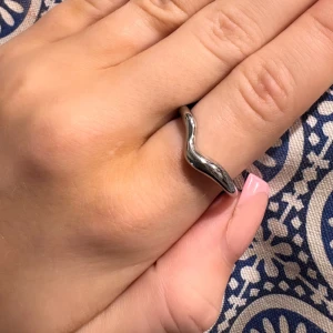 Silverfärgad vågig ring - Elegant silverfärgad ring med en unik vågig design.Ringen har en slät yta och är lätt att matcha med andra smycken.