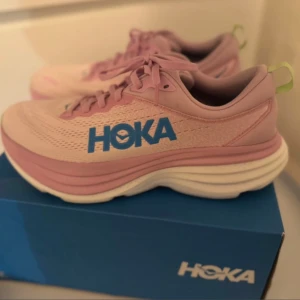 Rosa löparskor från Hoka - Säljer ett par rosa sneakers från Hoka med blå logga och gröna detaljer. Skorna har en tjock vit sula och snörning framtill. Perfekta för löpning / gym. Storlek 41,5 men passar mig med 39/40 då de är små i storleken.