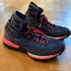 Adidas Adizero löparskor - Snygga Adidas Adizero löparskor i mörkblått och rosa med robusta sulor för bra grepp. Skorna har snörning och en hög ankel för extra stöd. Perfekta för löpning och utomhusaktiviteter.