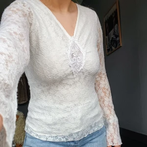 Vit spetsblus med v-ringning - Säljer en elegant vit spetsblus från kappalh med v-ringning och vackert broderad detalj framtill. Blusen har långa utsvängda ärmar. Passar utmärkt till både jeans och kjol. Perfekt för vårens och sommarens tillfällen! 🌸