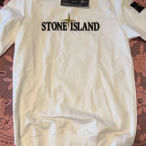Vit tröja från Stone Island - Säljer en stilren vit tröja från Stone Island med deras ikoniska logga broderad på framsidan. Tröjan har en klassisk passform och är perfekt för en avslappnad stil. Den är tillverkad i ett mjukt material som ger en bekväm känsla.