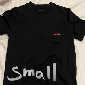 Svart t-shirt från Hugo - Säljer en stilren svart t-shirt från Hugo i storlek small. Den har en enkel design med korta ärmar och en liten röd Hugo-logga på bröstet. Perfekt för vardagsbruk. Säljs i 3 pack om man vill ha det för 350kr. Annars 150kr styck.