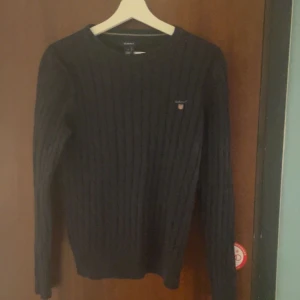 Svart stickad tröja från Gant - Säljer en stilren svart stickad tröja från Gant. Den har ett diskret broderat märke på bröstet och är perfekt för både höst och vinter. Tröjan är långärmad och har en klassisk passform. Perfekt för en snygg och bekväm look. Och köpt för 700kr!!
