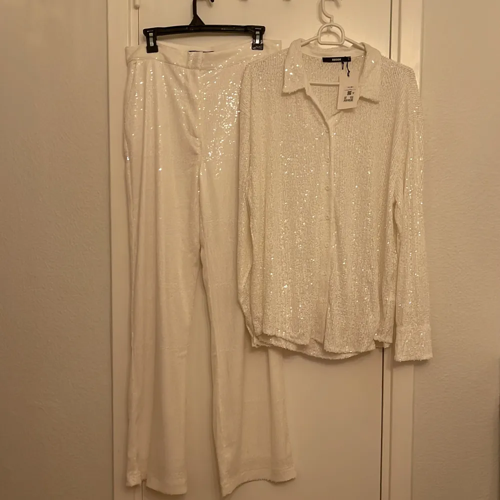 Säljer en superglittrig vit blus stl L från BIKBOK, perfekt för fest! Den har långa ärmar och är täckt med paljetter som verkligen fångar ljuset. Blusen har en klassisk krage och knappar framtill. Perfekt för att lysa upp vilken kväll som helst! Och säljer även med blusen matskandaler glittriga byxor stl 42 . Paidat.