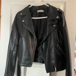 Svart skinnjacka från Glamorous - Säljer en snygg svart skinnjacka från Glamorous i storlek EUR 38. Jackan har en cool bikerstil med dragkedja och knappar. Perfekt för höst och vår, och funkar lika bra till fest som till vardags. Den är i nyskick och redo för nya äventyr!