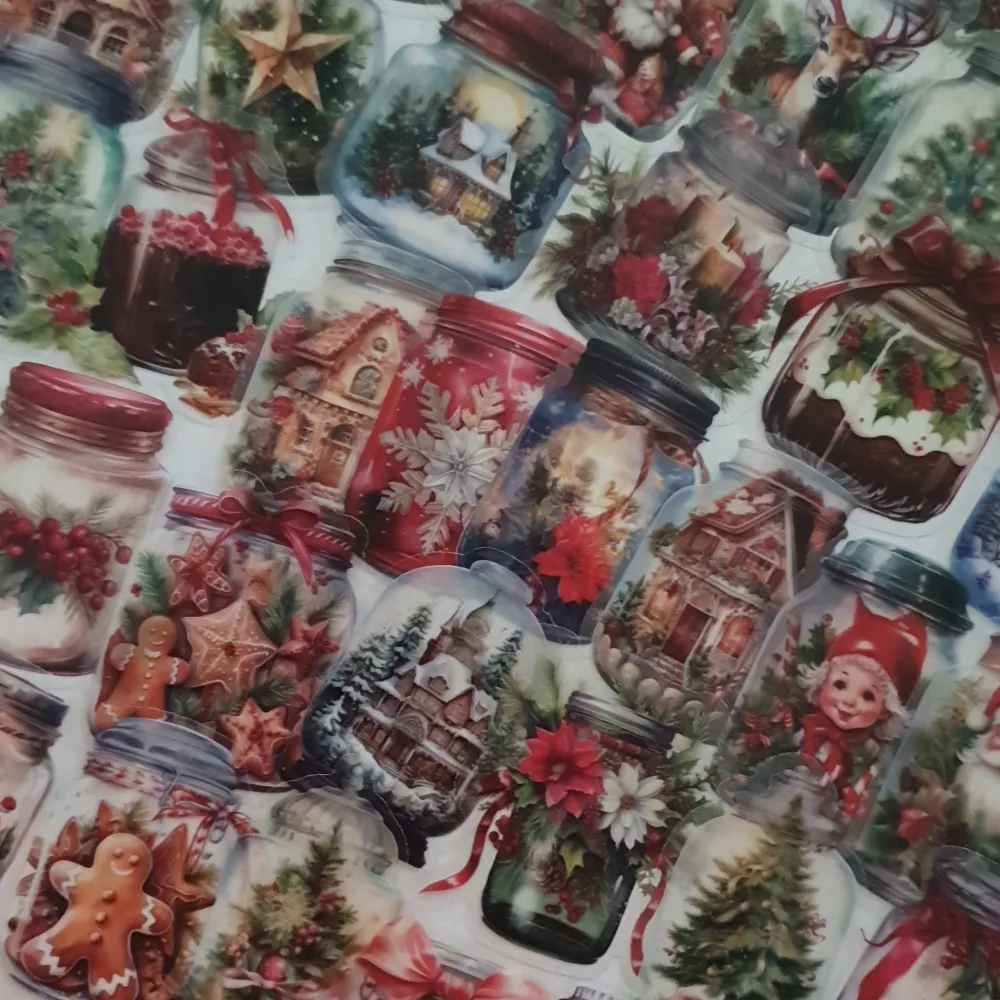 Ett ark med färgglada klistermärken som visar olika julmotiv inuti glasburkar. Motiven inkluderar snögubbar, pepparkakor, julgranar, renar och små hus täckta av snö. Perfekt för att dekorera julkort eller presenter. Klistermärkena har en mysig och traditionell julkänsla med mycket rött, grönt och vitt. Observera att skyddsplasten är tunn och kan vara lite krånglig att få lös.. Asusteet.