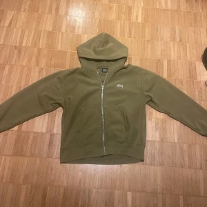 Olivgrön hoodie från Stussy - Säljer en olivgrön hoodie från Stussy i storlek S men jag skulle säga att den passar för någon med M. Perfekt till hösten. Skicket får avgöras själv av bilderna. Passar både till vardags och chillkvällar. 🧥Pris kan diskuteras!