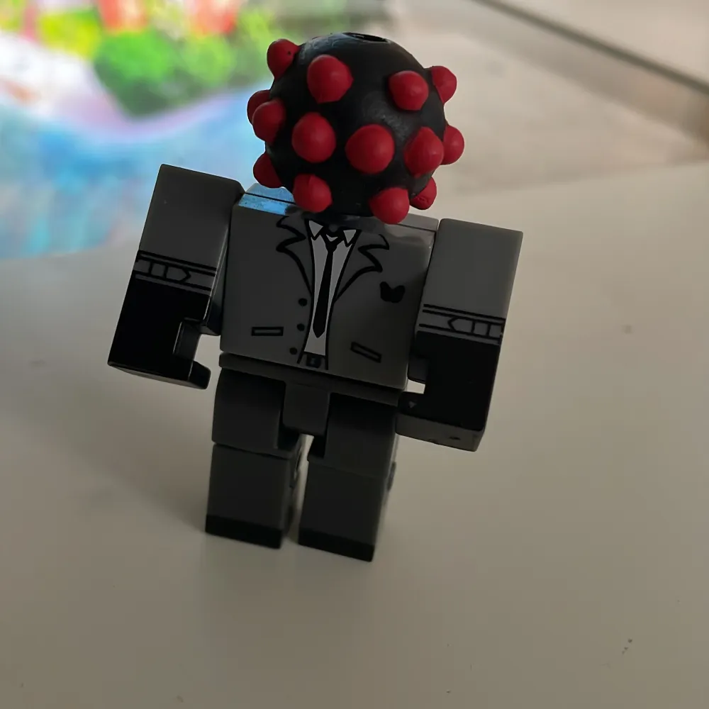 Cool Roblox-figur från Mystery Figure Series 10. Den har en unik design med ett grått kostymtryck och ett huvud som ser ut som en svart boll med röda prickar. Perfekt för samlare eller som en rolig leksak för . Övrigt.