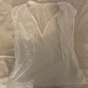 Vit blus i linne - Säljer en superfin vit blus i linne. Den har en avslappnad passform med v-ringning och knytband vid halsen. Perfekt för sommardagar eller en avslappnad vårlook. Blusen är i nyskick och redo för nya äventyr!