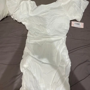 Kortklänning  - Klänning med puffiga armar och en snygg urringning i ryggen. Klänningen är aldrig använd, hade funkat perfekt som studentklänning!🥰