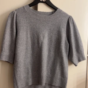 Grå stickad tröja med kort ärm - Mysig grå stickad tröja med korta ärmar och ribbade detaljer vid hals, ärmslut och nederkant. Från only ordinarie 