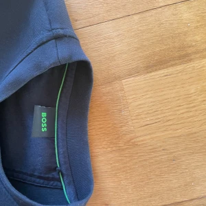 Mörkblå sweatshirt från Hugo BOSS - Snygg mörkblå sweatshirt från BOSS med stor vit logga framtill. Tröjan har rund halsringning, långa ärmar och ribbade muddar. Perfekt för en clean och stilren look. Materialet känns mjukt och bekvämt mot huden.